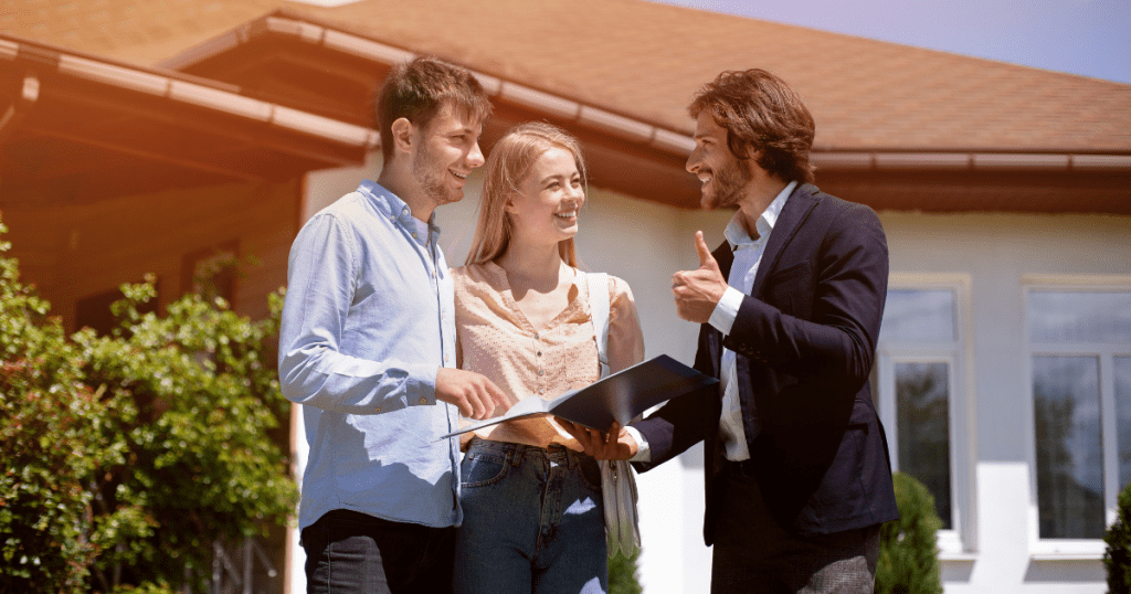 A young Australian couple smiles as they speak with a mortgage broker in front of their new home.
