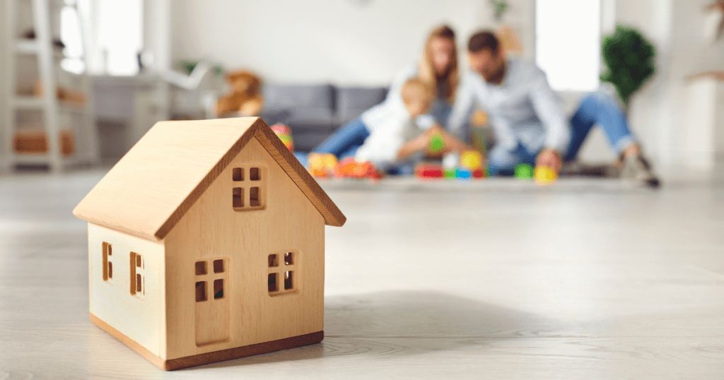A small house model symbolising property ownership with a family enjoying time together in the background